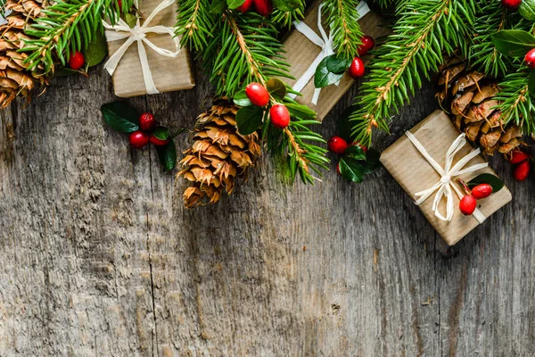 Jedlové větve s dekorace - červená holly šišky a dárkové boxy. Vánoční pozadí, pohled shora — Stock fotografie