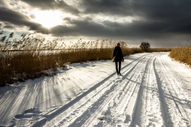 Yolda kar ile kış, peyzaj, romantik bir sahne karanlık gökyüzü ile gün batımına yürüyen yalnız kadın