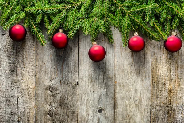 Biglietto di Natale rustico con ornamenti - bagattelle rosse appese a rami di abete su sfondo di legno — Foto Stock