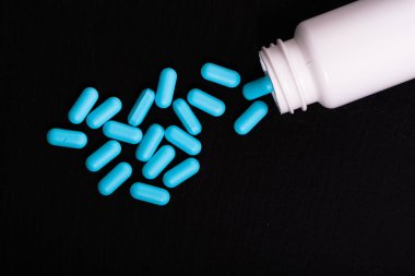 Bir şişe ilaç ağrı kesici mavi hap. Siyah bir zemin üzerine ilaçlar