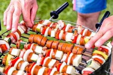 Barbekü Izgara yemek ızgara, şiş ile sebze ve sosis, Barbekü çimenlerin üzerinde hazırlanıyor eller