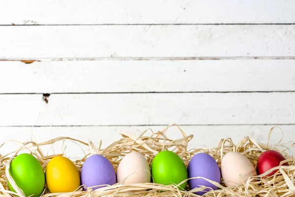 Huevos de Pascua en nido sobre fondo de madera, tablas blancas con grupo de huevos en paja — Foto de Stock