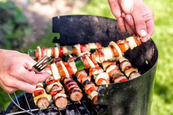 Vegetables and meat kebabs grilled over the coals on barbecue grill, people grilling food outdoors — Stock Photo, Image