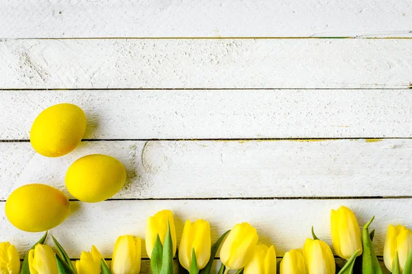 Tulipes de printemps et oeufs de Pâques jaunes sur fond de bois blanc — Photo