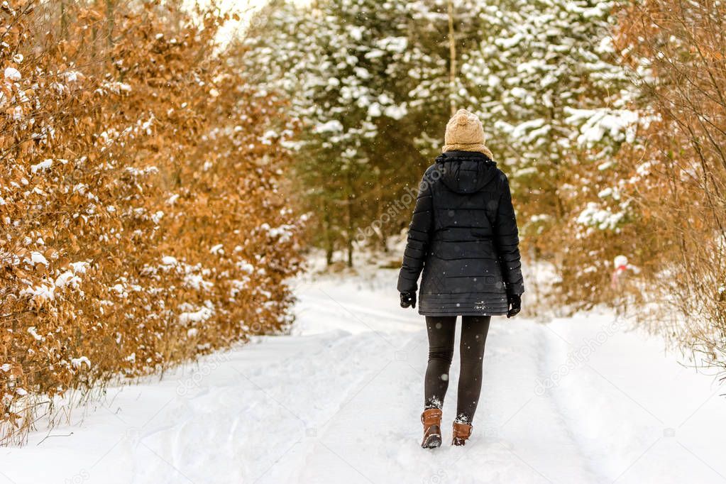 Woman walking on a winter snow road, girl in warm winter clothes, back view