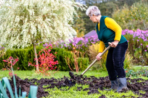 Agricoltore operaio nel giardino autunnale. Concime organico per concimazione del terreno, preparazione del terreno per la semina in primavera, concetto di agricoltura biologica . — Foto Stock