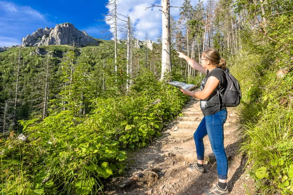 Woman hiker in mountains. Tourist with a map, walking on a hiking trail leading to the top of mountain.