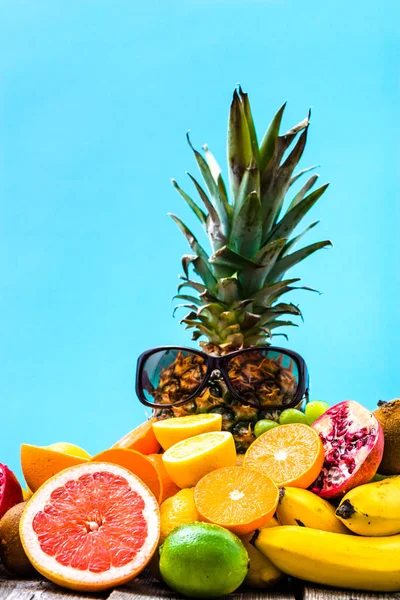 Summer background with fruits, tropical fresh fruit cut, orange, half of grapefruit, pineapple and sunglasses on blue background