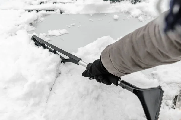 Kvinnan städar bilen från snön med pensel. Människor i snöigt kallt väder på vintern och transportkoncept. — Stockfoto