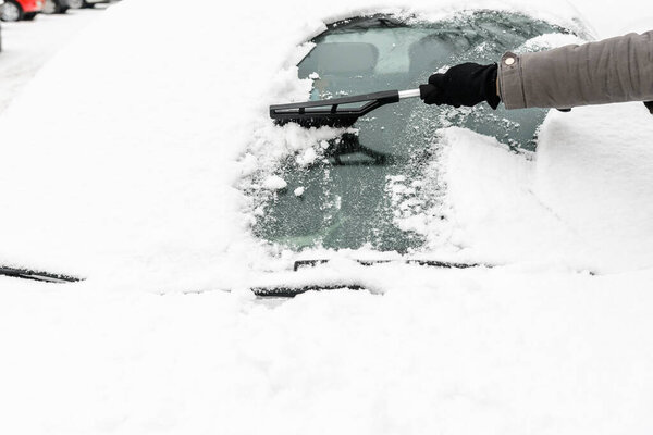 Woman cleaning car from the snow with brush. People in snowy cold weather in winter and transportation concept.