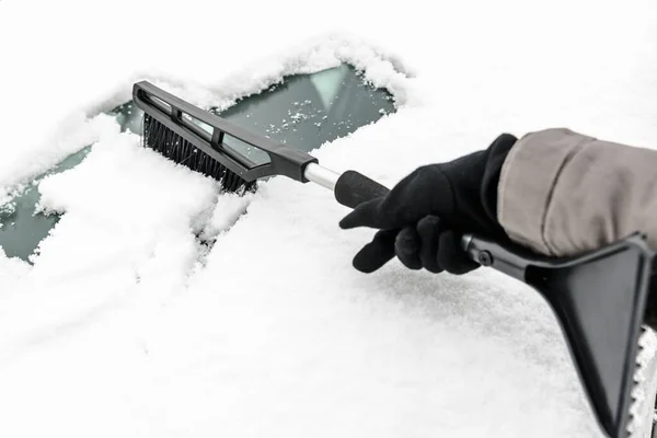 Kvinnan städar bilen från snön med pensel. Människor i snöigt kallt väder på vintern och transportkoncept. — Stockfoto