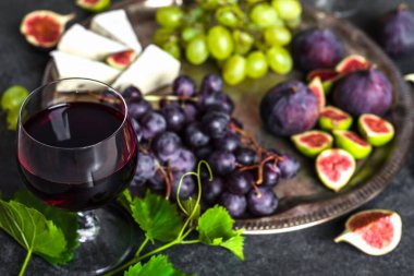 Peynirli, üzümlü ve incirli bir kadeh kırmızı şarap. Tabakta Fransız yemeği.