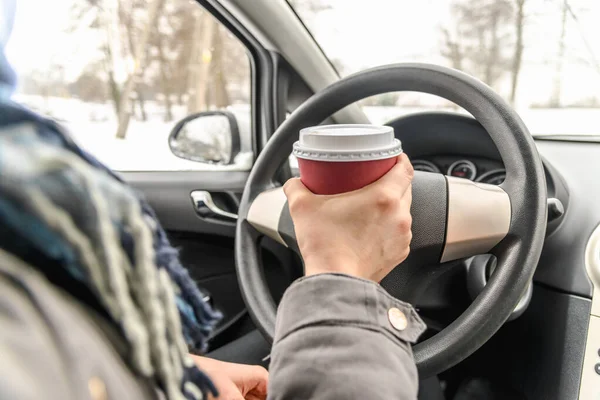 Motorista bebendo café no carro, dirigindo e segurando um volante e xícara de bebida quente no dia frio de inverno com neve atrás da janela — Fotografia de Stock