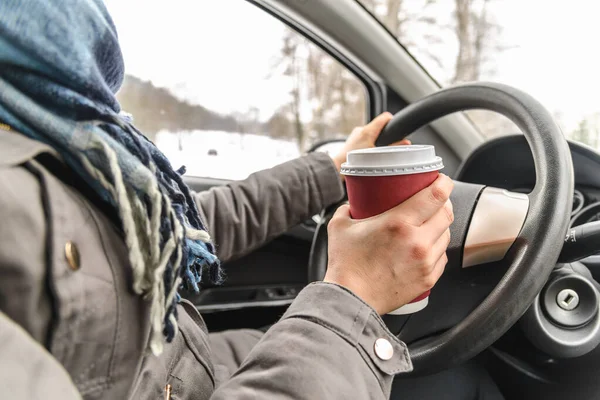 Motorista bebendo café no carro, dirigindo e segurando um volante e xícara de bebida quente no dia frio de inverno com neve atrás da janela — Fotografia de Stock