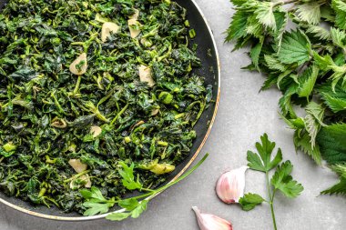 Yeşil sebze pişiriyorum. Sağlıklı yemek, yeşil ısırgan otlu vejetaryen pesto ve taze ısırgan otu. Kızarmış sarımsaklı yapraklar ve tavada baharatlar..