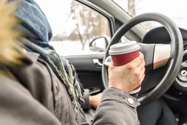 Motorista bebendo café no carro, dirigindo e segurando um volante e xícara de bebida quente no dia frio de inverno com neve atrás da janela — Fotografia de Stock