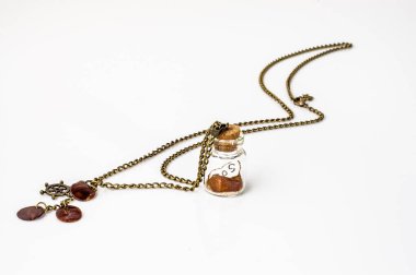 Pendant made with glass bottle, antique gold chain and amber isolated on white background. Handmade jewelry.