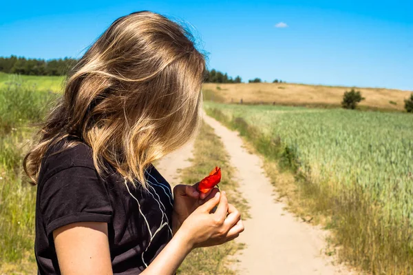 Młoda kobieta w rolniczej scenerii trzyma w ręku kwiat maku — Zdjęcie stockowe