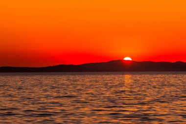 Deniz üzerinde güzel turuncu gün batımı, dağların ufuklarında güneş, Zadar, Dalmaçya, Hırvatistan ve Avrupa plajlarından manzara