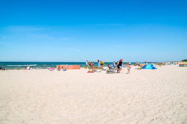 LEBA, POLAND - 09 Haziran 2019: plajdaki insanlar, deniz ve mavi gökyüzünde güneşlenen yaz tatili konsepti