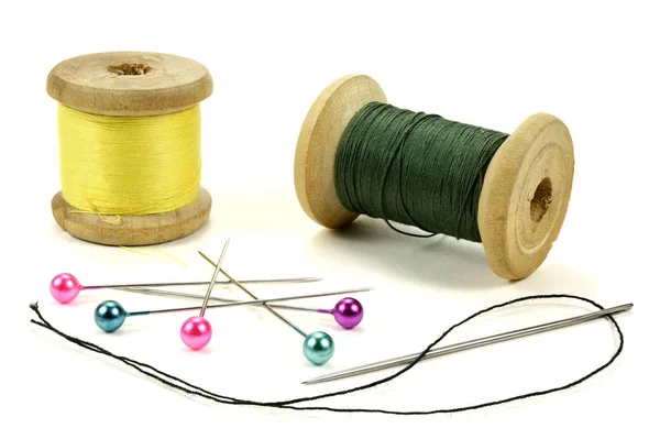 Bobinas de madera con hilos, alfileres y aguja para coser sobre fondo blanco —  Fotos de Stock