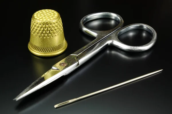 Dedal, tesoura e agulha sobre um fundo preto — Fotografia de Stock