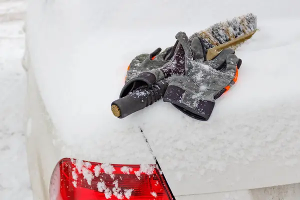 Brosse à neige et gants d'hiver sur le capot d'une voiture enneigée — Photo