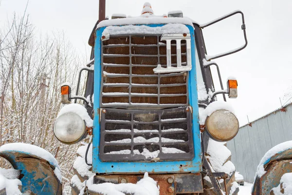 Fragmento de la parte delantera de un viejo tractor cubierto de nieve sobre un fondo nublado cielo de invierno — Foto de Stock