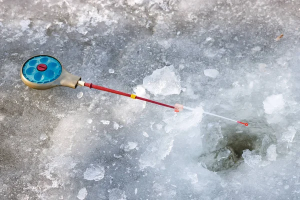 Рыболовный стержень для зимней рыбалки лежит на льду возле ямы — стоковое фото