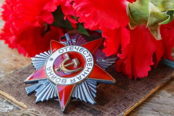Soviet order of Patriotic War (inscription Patriotic war) with red carnations on an old wooden table. May 9 day of victory in the great Patriotic war of 1941-1945 — Stock Photo, Image