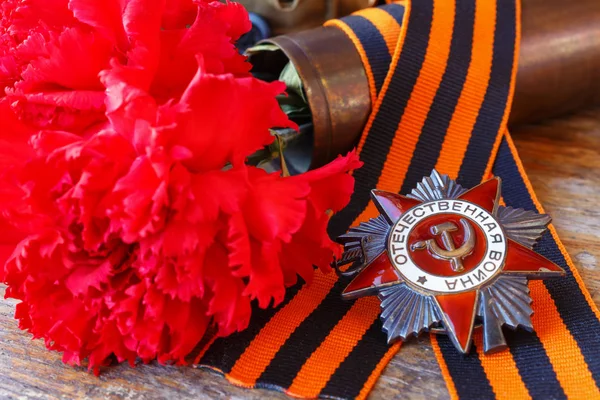 Soviet order of Patriotic war with St. George\'s ribbon and red carnations on an old wooden table. May 9 Victory day in the great Patriotic war of 1941-1945