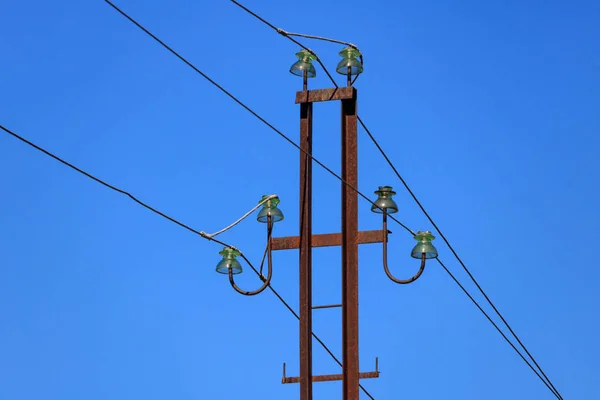 Roestige metalen elektriciteitsleiding ondersteunen met draden en glazen isolatoren close-up tegen de blauwe hemel — Stockfoto