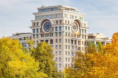 Moskova, Rusya - 03 Ekim 2019: Güneşli bir sonbahar gününde, yaprakları renkli ağaçlara karşı çatı altında büyük yuvarlak pencereleri olan modern konut binasının köşe kulesinin manzarası