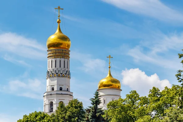 Moscú, Rusia - 02 de junio de 2019: Domos dorados de Iván el Gran Campanario y el campanario de Uspenskaya contra el cielo azul con nubes blancas y árboles verdes a la luz del sol. Arquitectura del Kremlin de Moscú — Foto de Stock