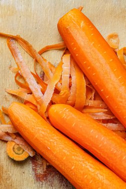 Tahta kesme tahtasındaki deriyi soyduktan sonra parlak turuncu, sulu havuçlar.