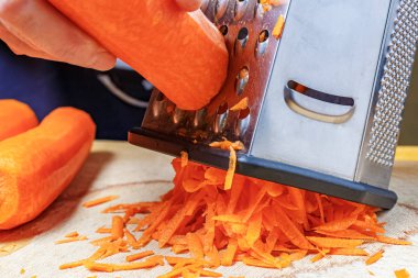 Paslanmaz çelik rendeleyicinin üzerinde taze turuncu havuç rendeliyor.