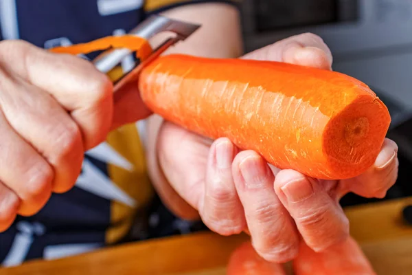Горілка для овочів і фруктів у жіночих рукостисканнях. Жінка чистить свіжу соковиту моркву. — стокове фото