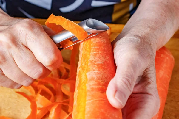 Очистка свежей сочной морковки очистителем для овощей и фруктов крупным планом — стоковое фото