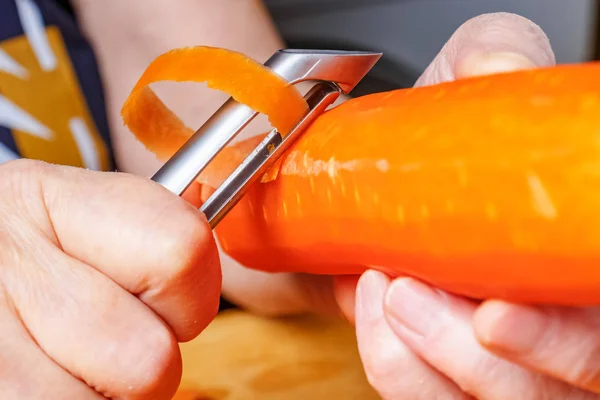 Woman peeling fresh juicy carrot by peeler for vegetables and fruits close-up