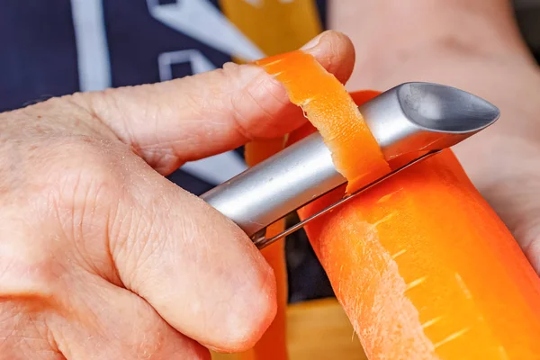 Peeling fresh juicy carrot by peeler for vegetables and fruits close-up