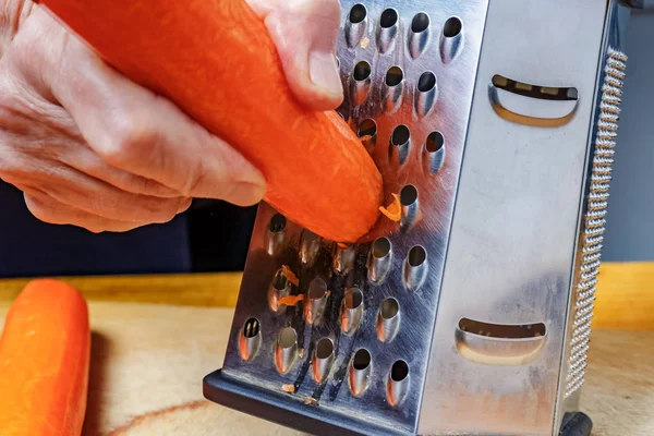 Женская ручная решетка из свежей ярко-оранжевой моркови на терке из нержавеющей стали — стоковое фото