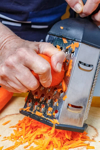 Жіночі руки терти свіжу соковиту моркву на тертці з нержавіючої сталі — стокове фото