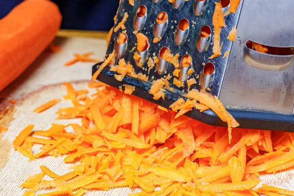 Терка з нержавіючої сталі з тертою соковитою морквою крупним планом на дерев'яній обробній дошці — стокове фото