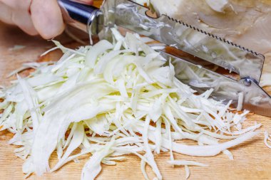 Ahşap kesme tahtasının üzerinde taze, sulu, sulu, beyaz bir lahana. Kadının elinde paslanmaz çelik bıçak ve lahana kafaya karşı.