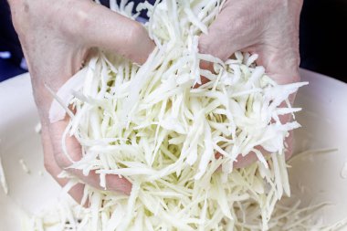 Kadın elleri metal kasede parçalanmış lahana ile tuzu karıştırıyor.