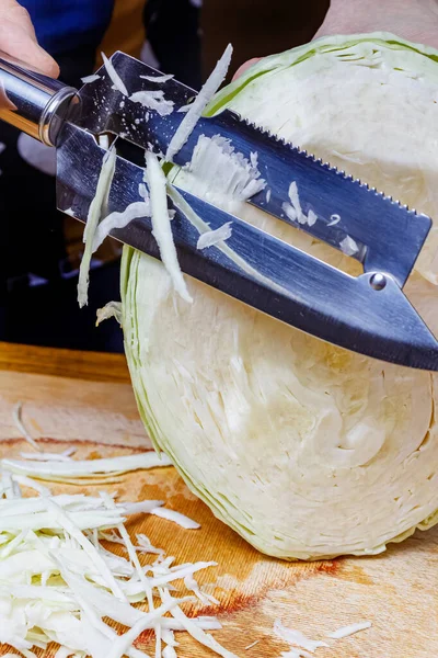 Резка головы свежей сочной белой капусты ножом для измельчения на деревянной доске — стоковое фото