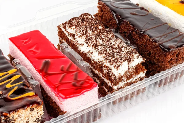 Různé Tiramisu koláče v průhledné plastové krabici na bílém pozadí zblízka — Stock fotografie