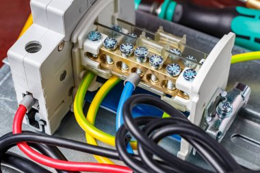 Automatic circuit breaker and wire terminal on DIN rail connected by colored wires with cord end insulated ferrules. Assembled electrical panel close-up