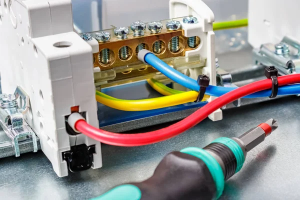 Connected by colored wires electrical equipment against screwdriver with colored plastic handle close-up. Electrical panel assembling — Stock Photo, Image
