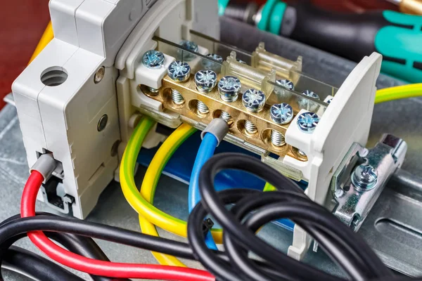 Automatic circuit breaker and wire terminal on DIN rail connected by colored wires with cord end insulated ferrules. Assembled electrical panel close-up